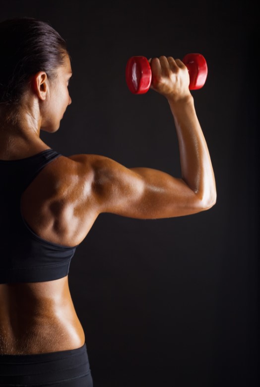 Young woman holding a dumb bell and flexing muscles