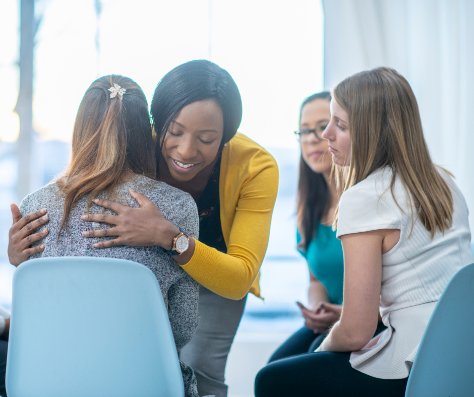 One woman comforting another in a group support setting.