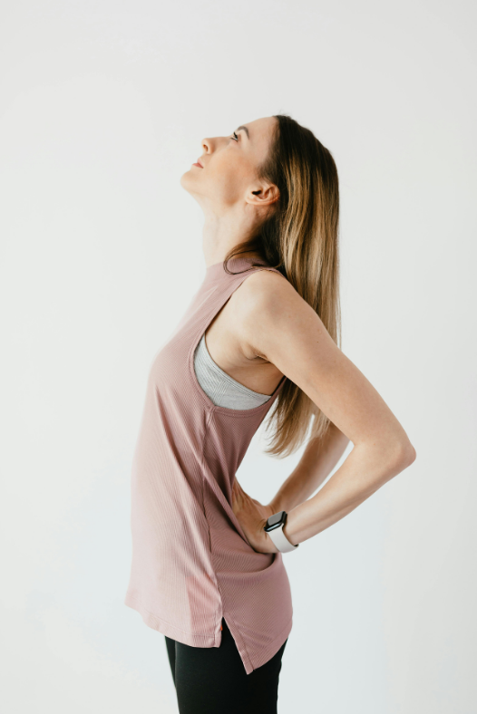 A young woman standing sideways holding her lower back in pain.