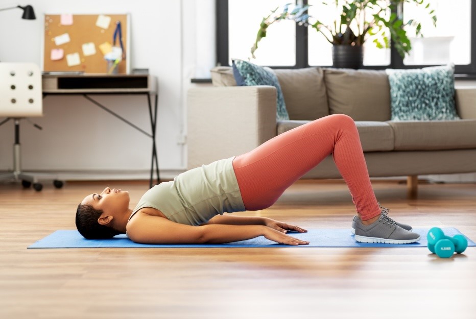 Young woman on a blue yoga mat demonstrating a bridge pose as good pelvic floor exercise. 