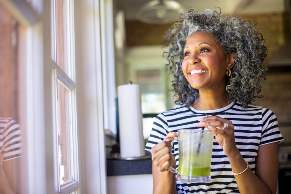 A smiling middle-aged woman drinking a green smoothie to manage hormone imbalance through a healthy lifestyle.
