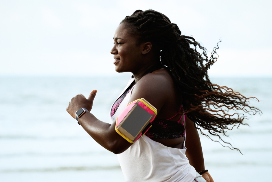 Young woman running by the sea with smart phone in arm band.