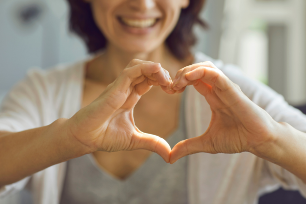 A woman in soft focus making a healthy heart shape with her hands.