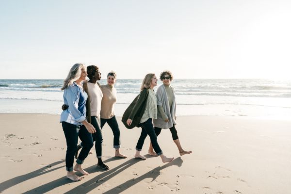 Women walking together on a beach for movement and community to control perimenopause hormones.