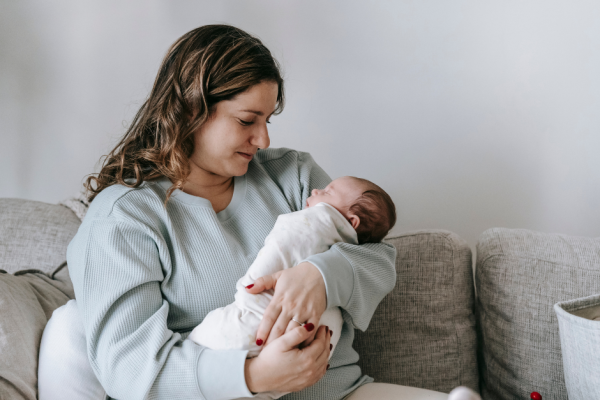 Postpartum young mother sitting on a sofa with a newborn baby.