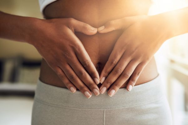 Woman's torso with hands forming a heart over lower abdomen.