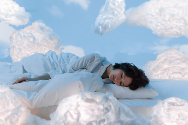 Woman sleeping on white pillows amongst fluffy white clouds